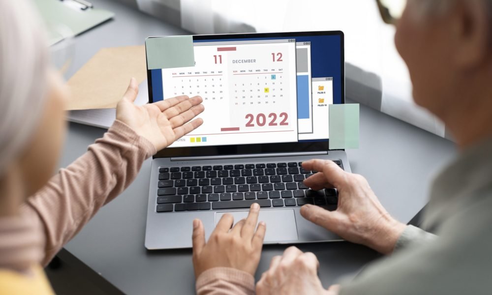 arabic-woman-teaching-senior-man-use-calendar-laptop-sitting-desk